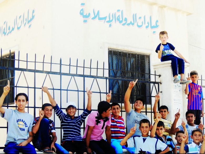 Un grop de mainatges iraquians auçan lo det en soslinhant l’unicitat de Dieu davant un espital de l’Estat Islamic en Iraq e Siria